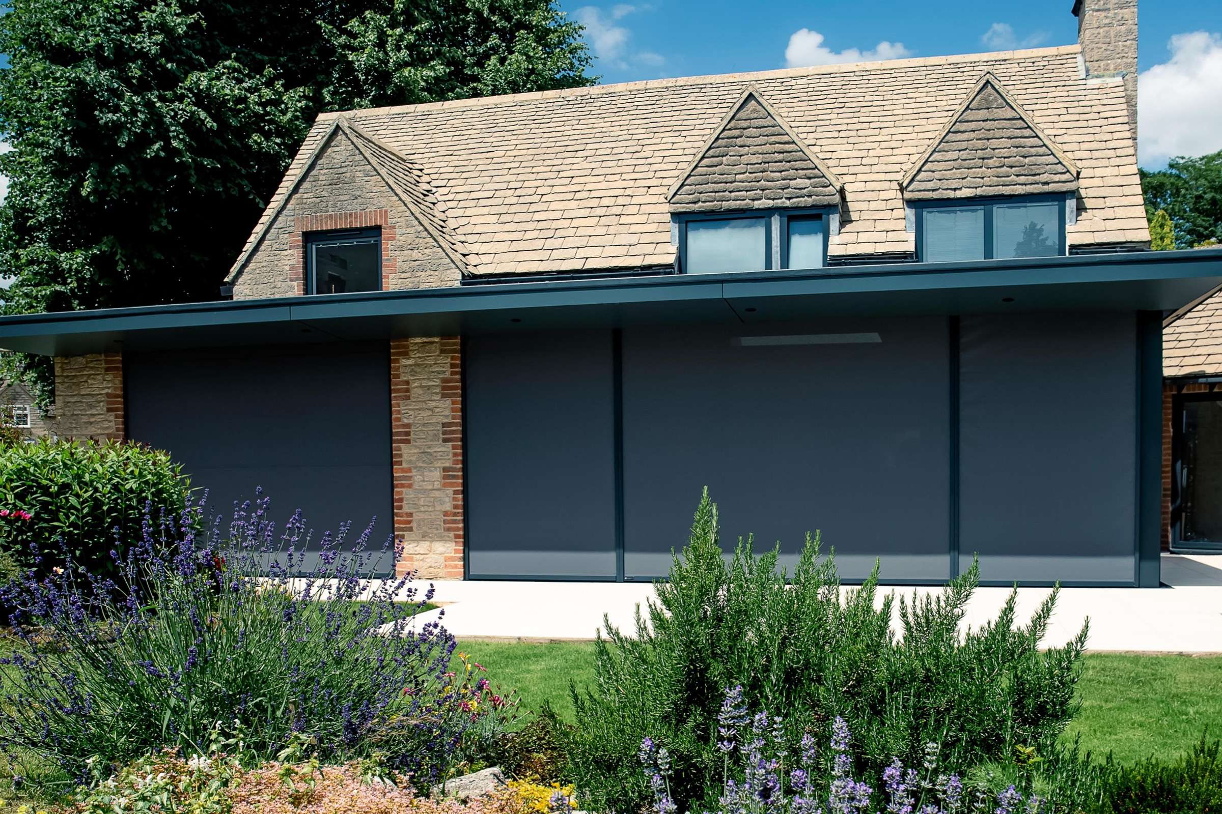 External roller blinds on a modern property with green shrubs and grass in the foreground