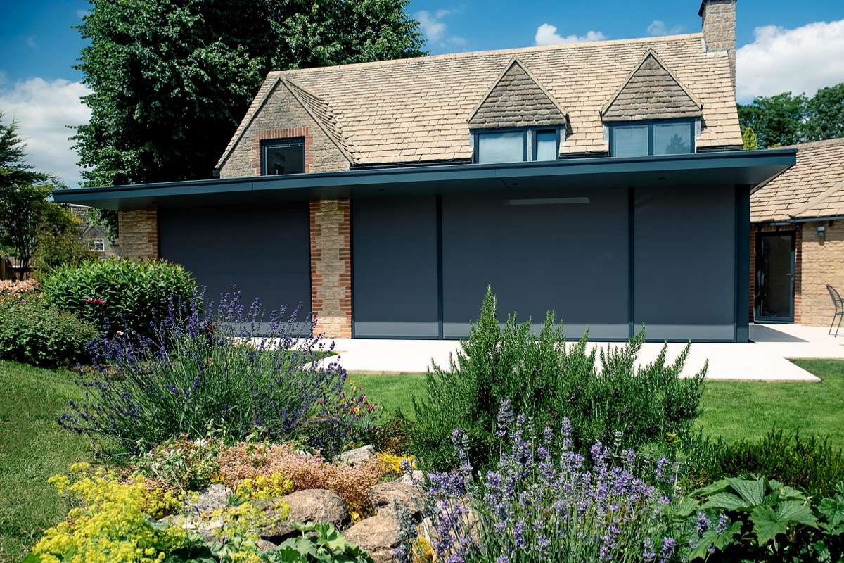 External roller blinds on a modern property with green shrubs and grass in the foreground